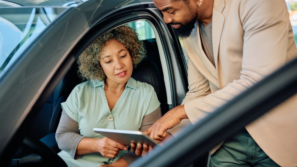 Car sales person showing a customer a tablet with information about the vehicle