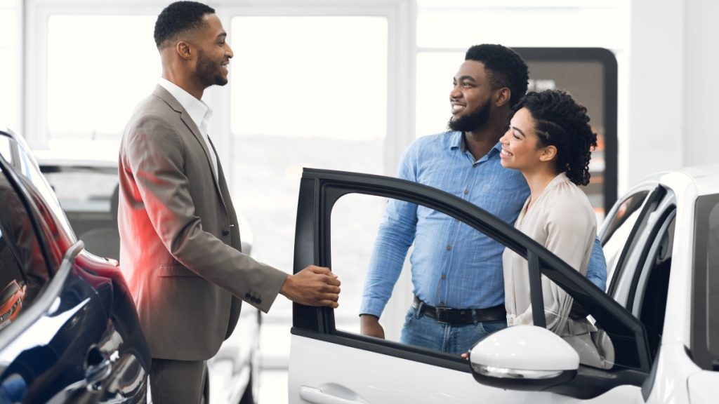 Two people buying a car at a dealership with the sales person next to them